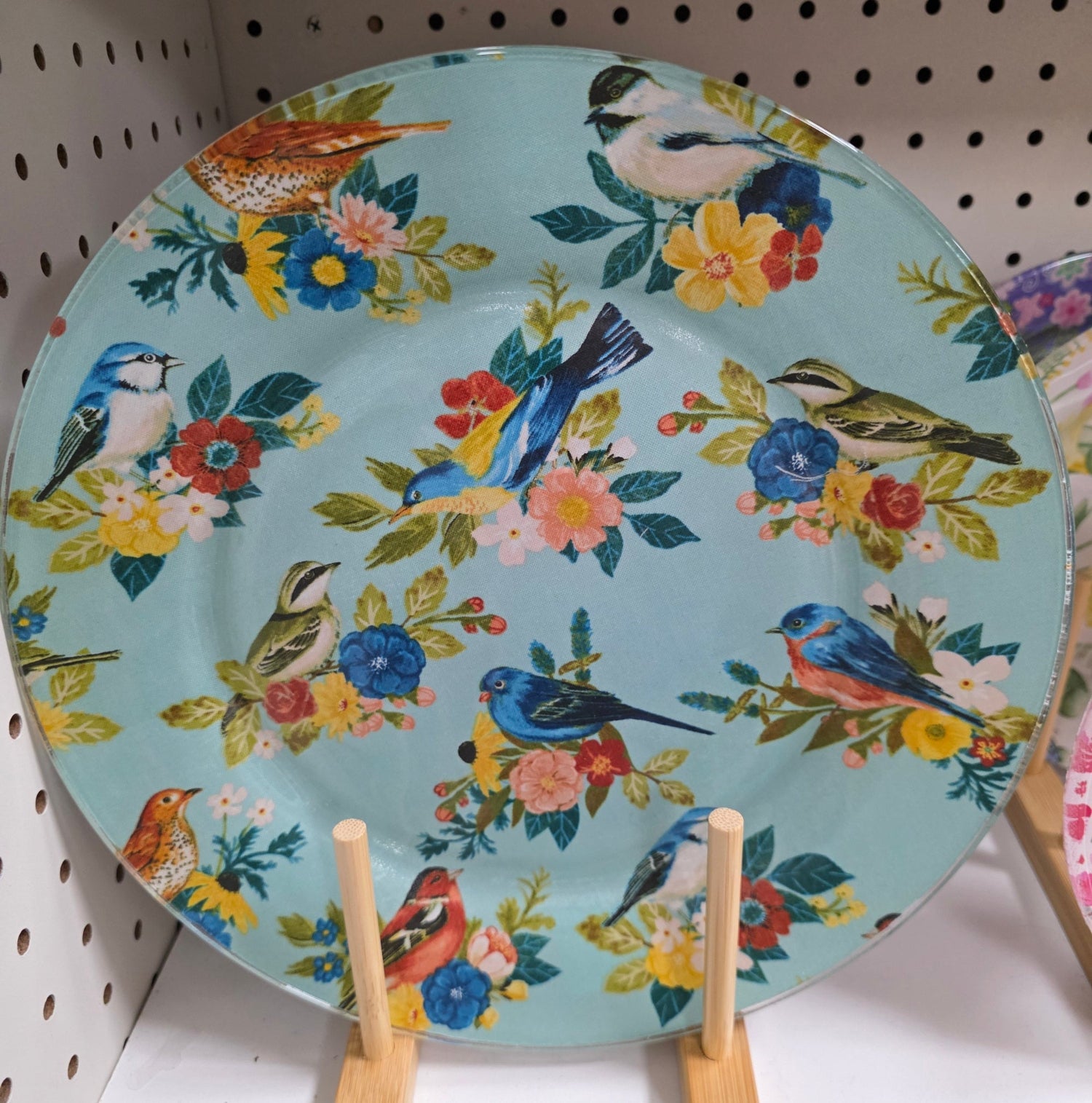 Decorative plate with floral and bird design on a pegboard