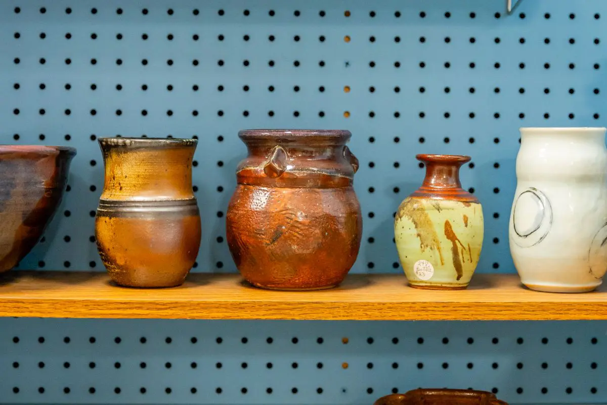 Three vases are on a shelf in front of a wall.