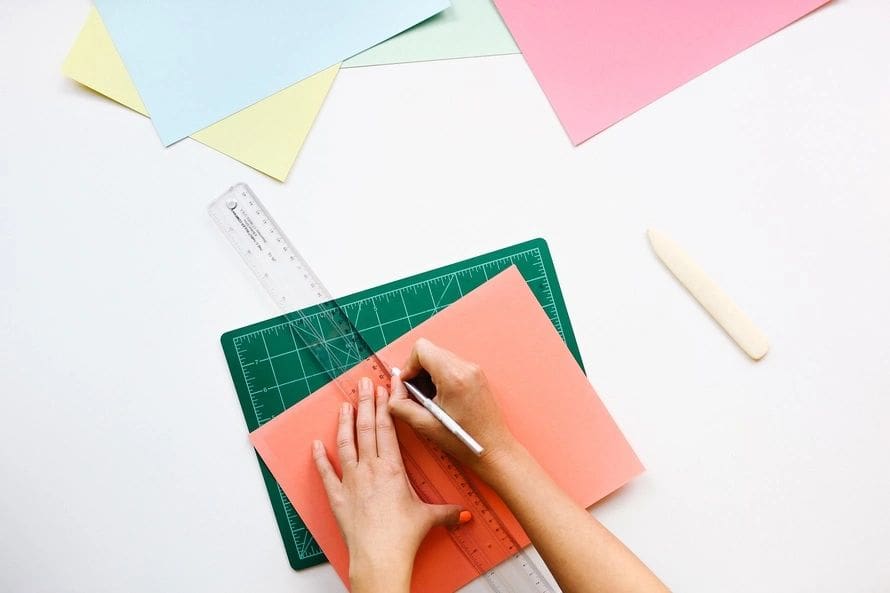 Hands cutting paper with ruler on cutting mat.