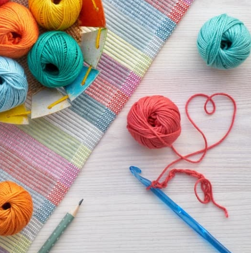 Colorful yarn balls, crochet hook, heart shape.